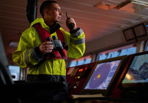 Navigator. pilot, captain as part of ship crew performing daily duties with VHF radio, binoculars on board of modern ship with high quality navigation equipment on the bridge on sunrise.